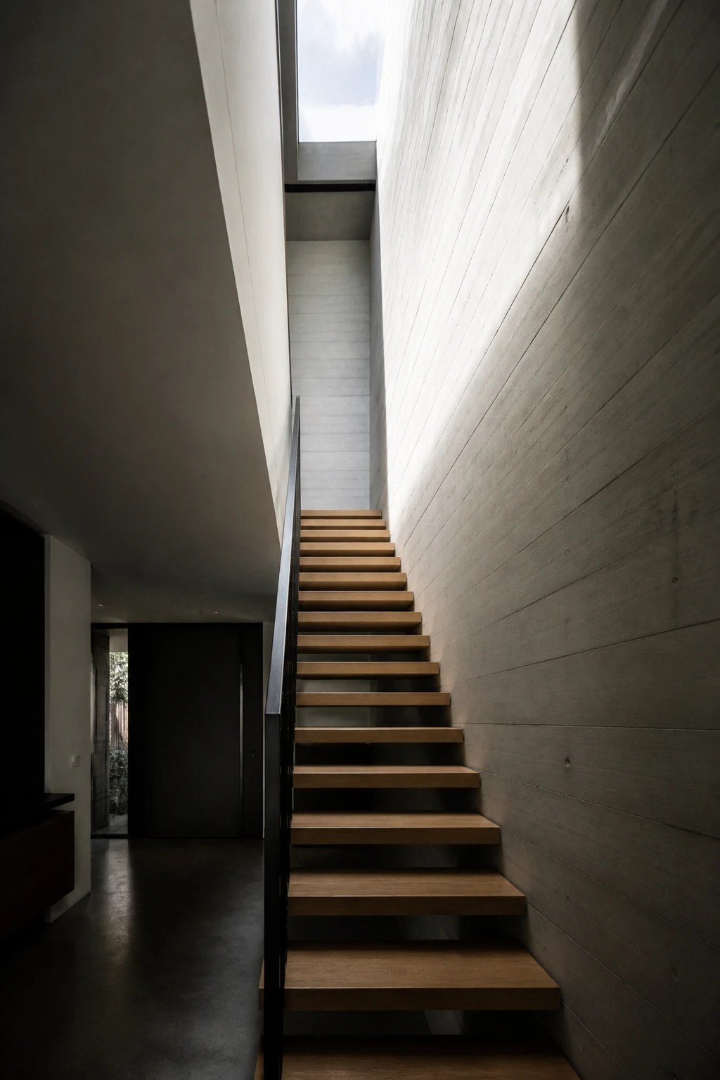Casa Pilar: escalera de peldaños de roble en voladizo contra un muro de hormigón, iluminada desde un lucernario cenital.
